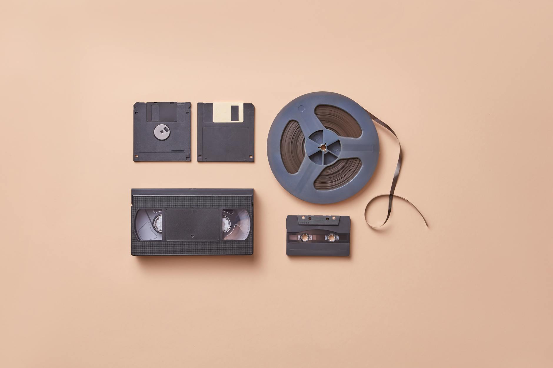 A collection of vintage media storage formats including VHS, cassette, and floppy disks on a beige background.
