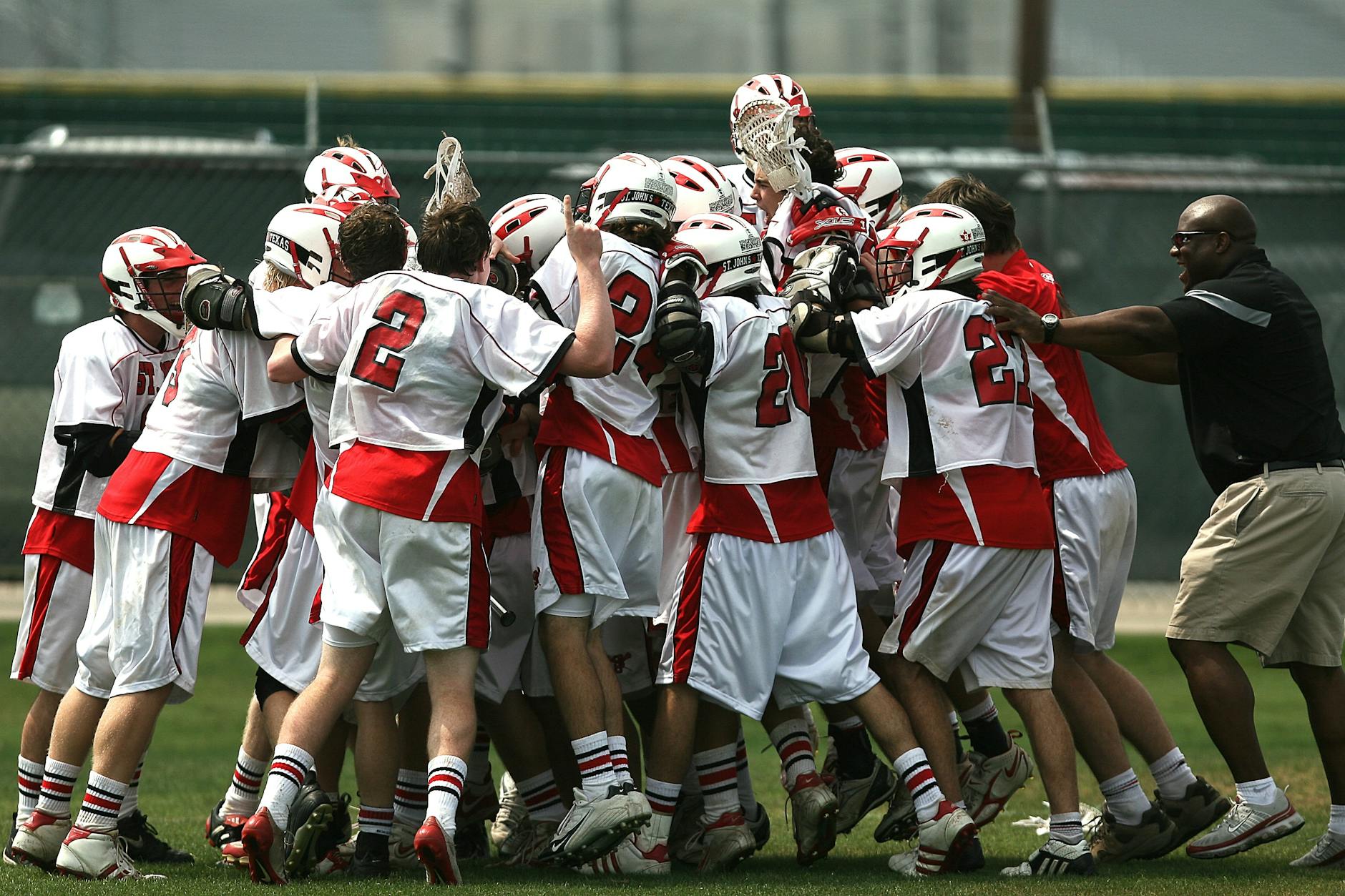 A group of lacrosse players and their coach celebrating a victory on the field.
