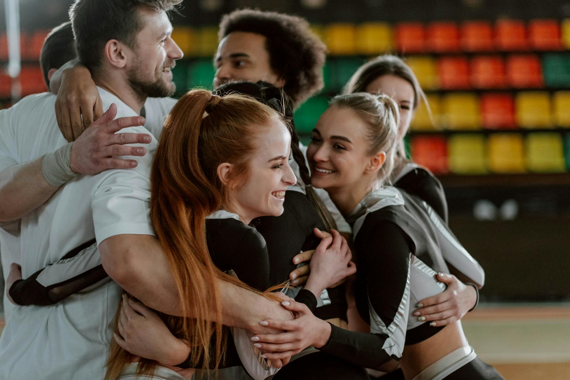 A joyful group of cheerleaders hugging, celebrating a successful performance indoors.