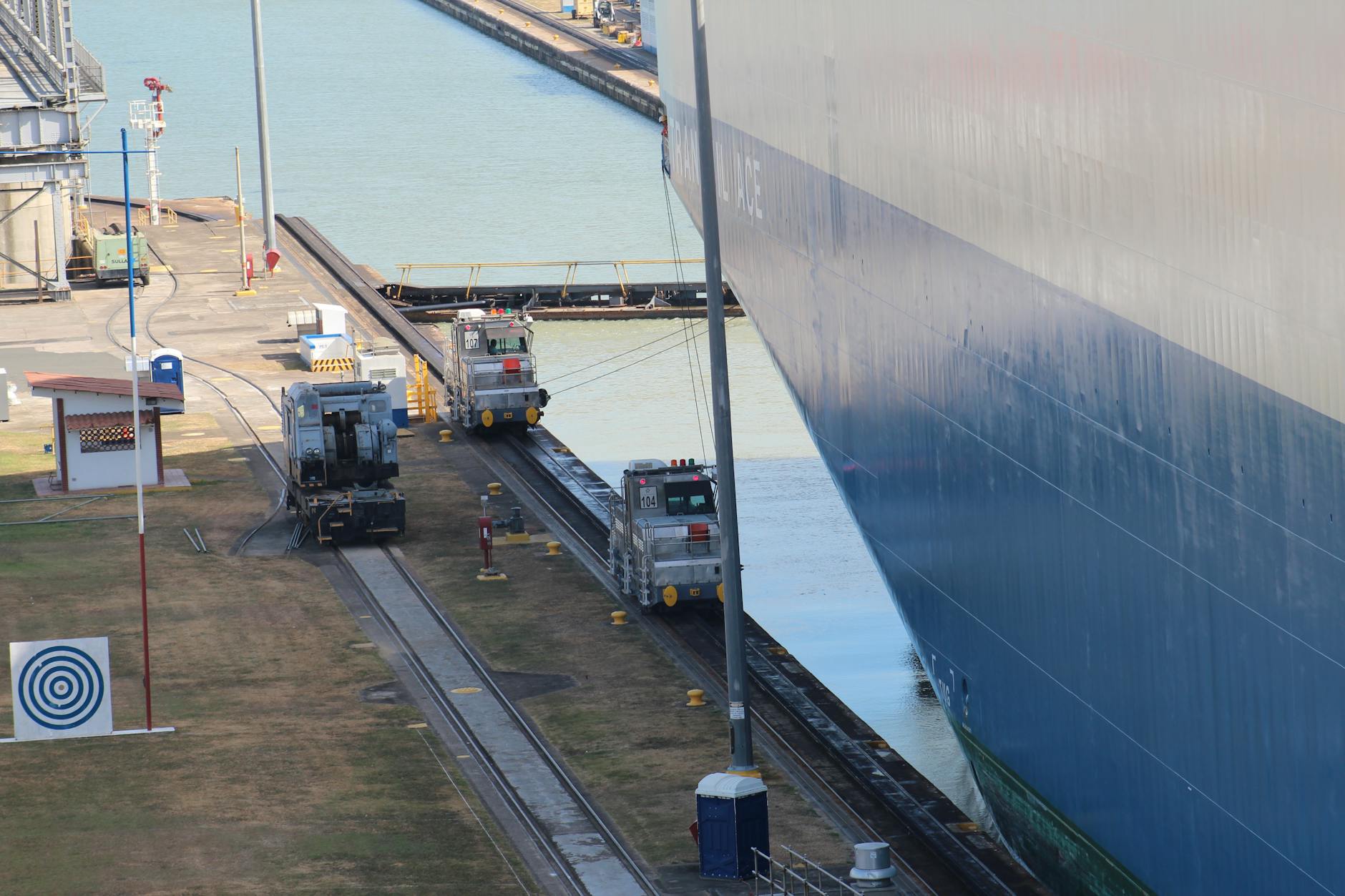 A large ship navigates through a canal with industrial machinery guiding its path.