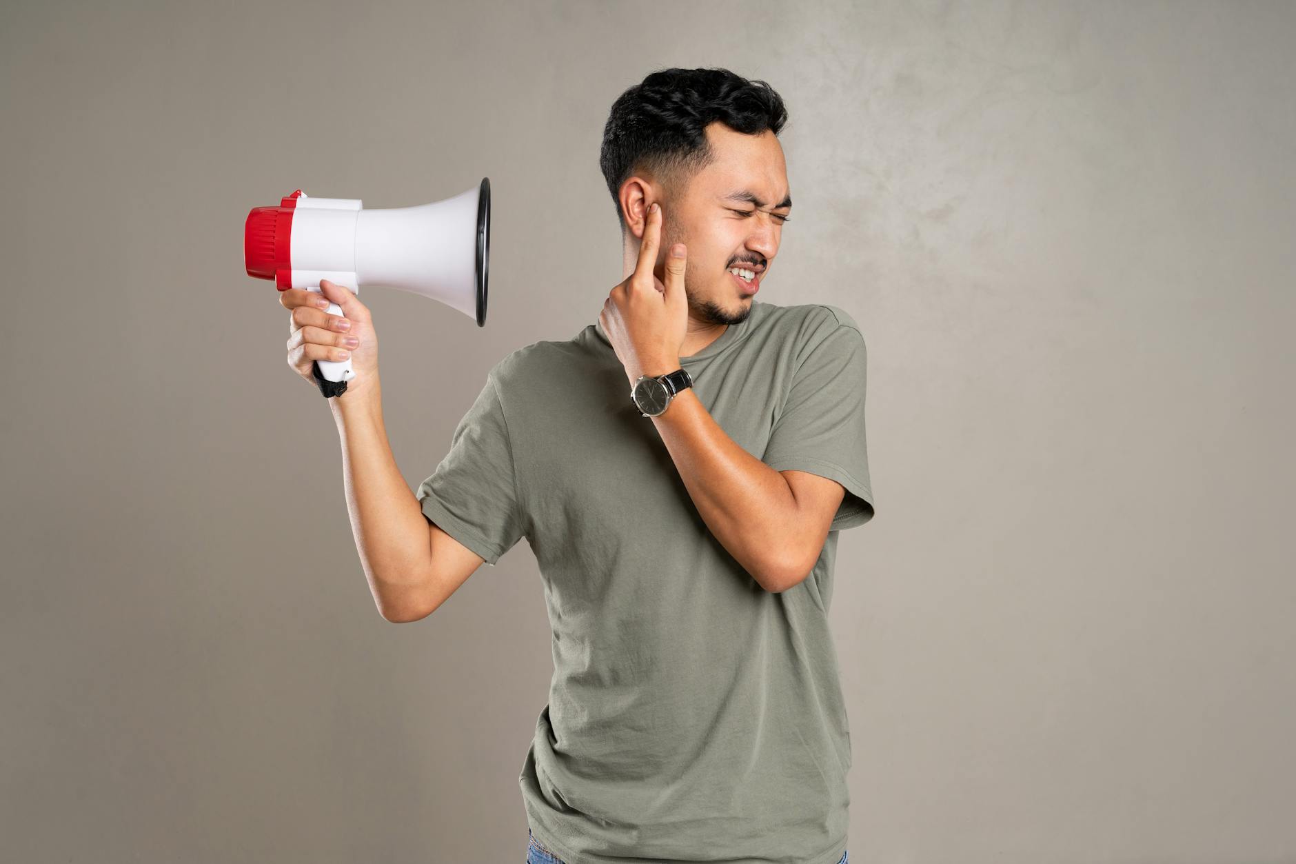 A man with a megaphone holding ear in discomfort, representing noise pollution or loud sounds.