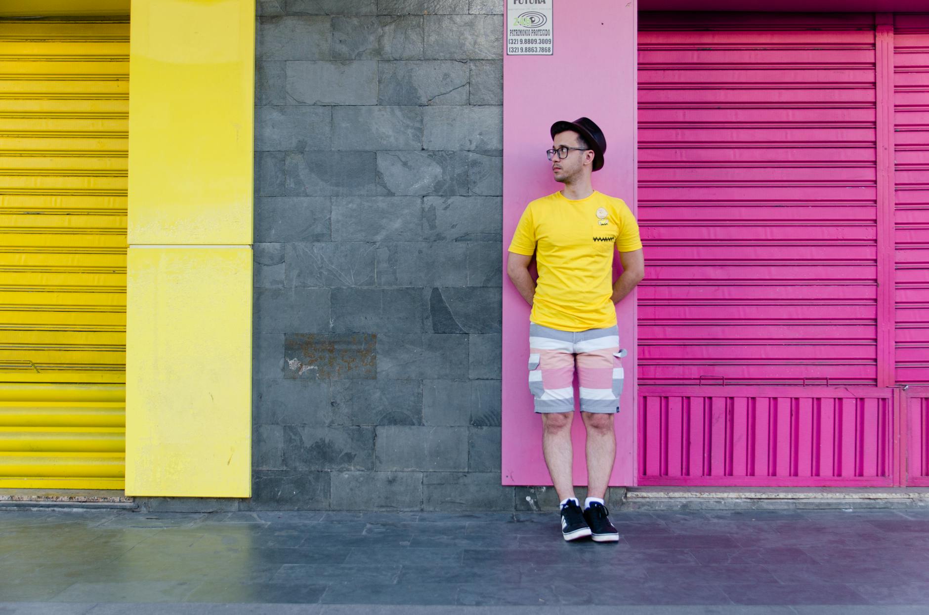 A stylish man stands against a vibrant yellow and pink backdrop in Juiz de Fora, capturing modern urban fashion.