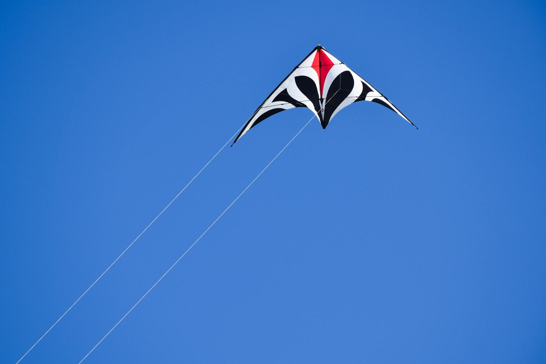 A vibrant kite with geometric patterns flying high against a clear blue sky.