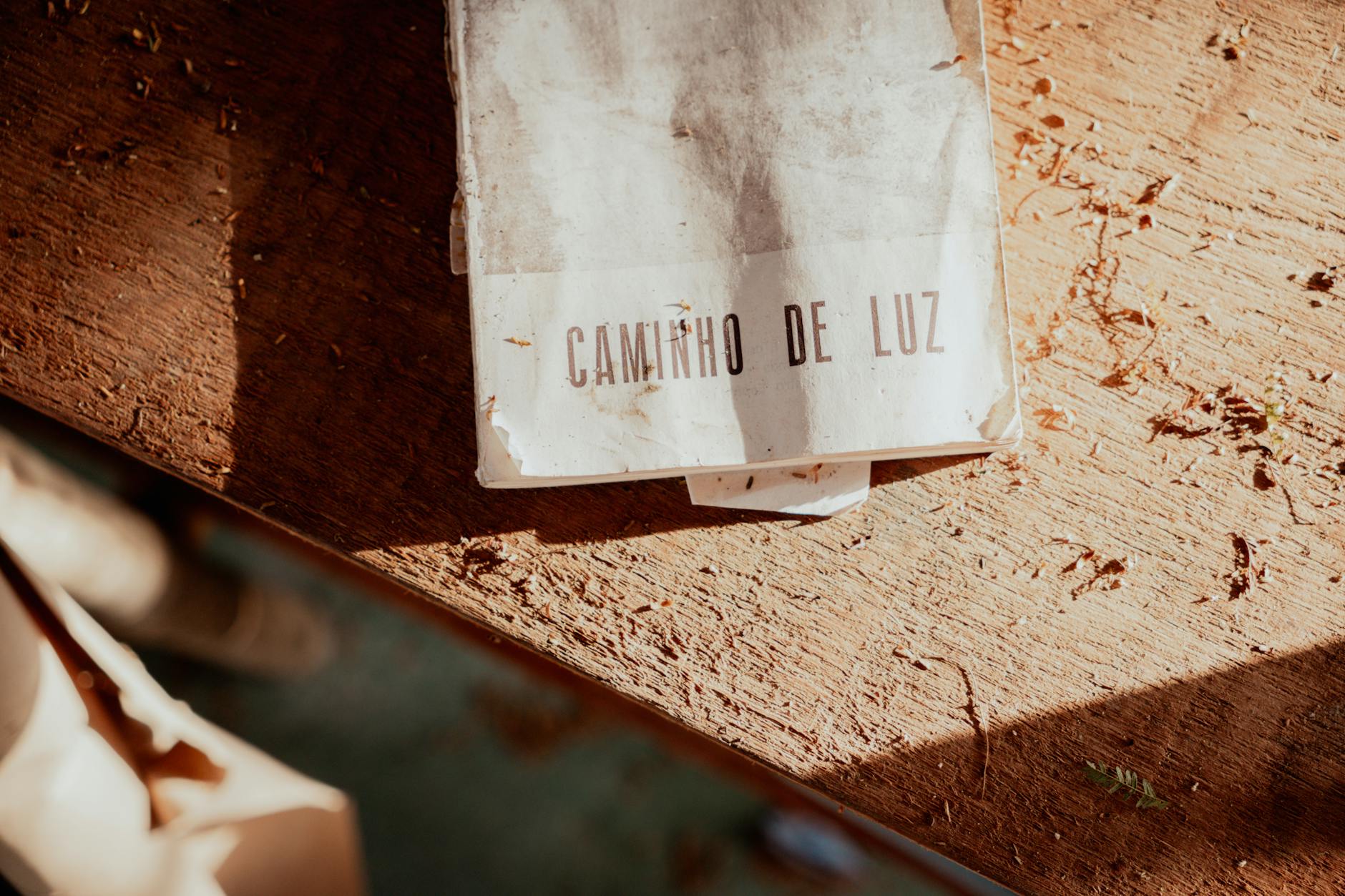A worn paper titled 'Caminho de Luz' on a rustic wooden table, lit warmly.