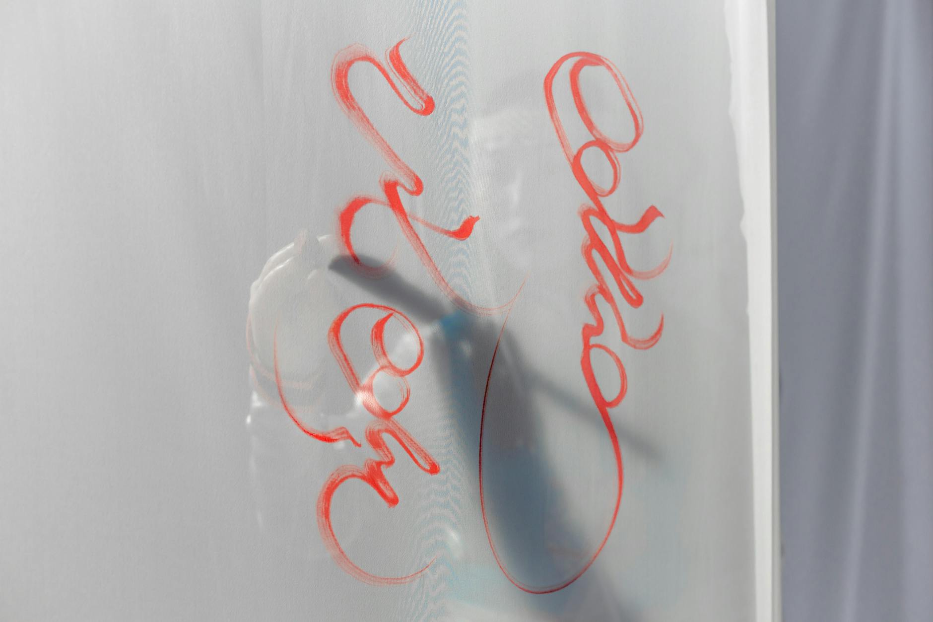Artistic red calligraphy strokes on a semi-transparent surface create an abstract play of shadows and light.
