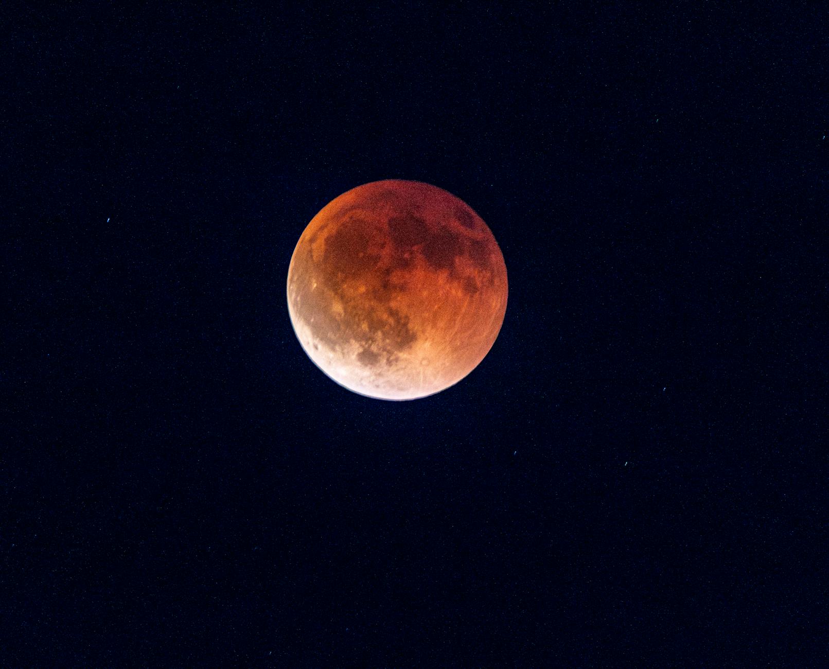 Capture of a total lunar eclipse displaying the moon in a striking red hue against a dark night sky.