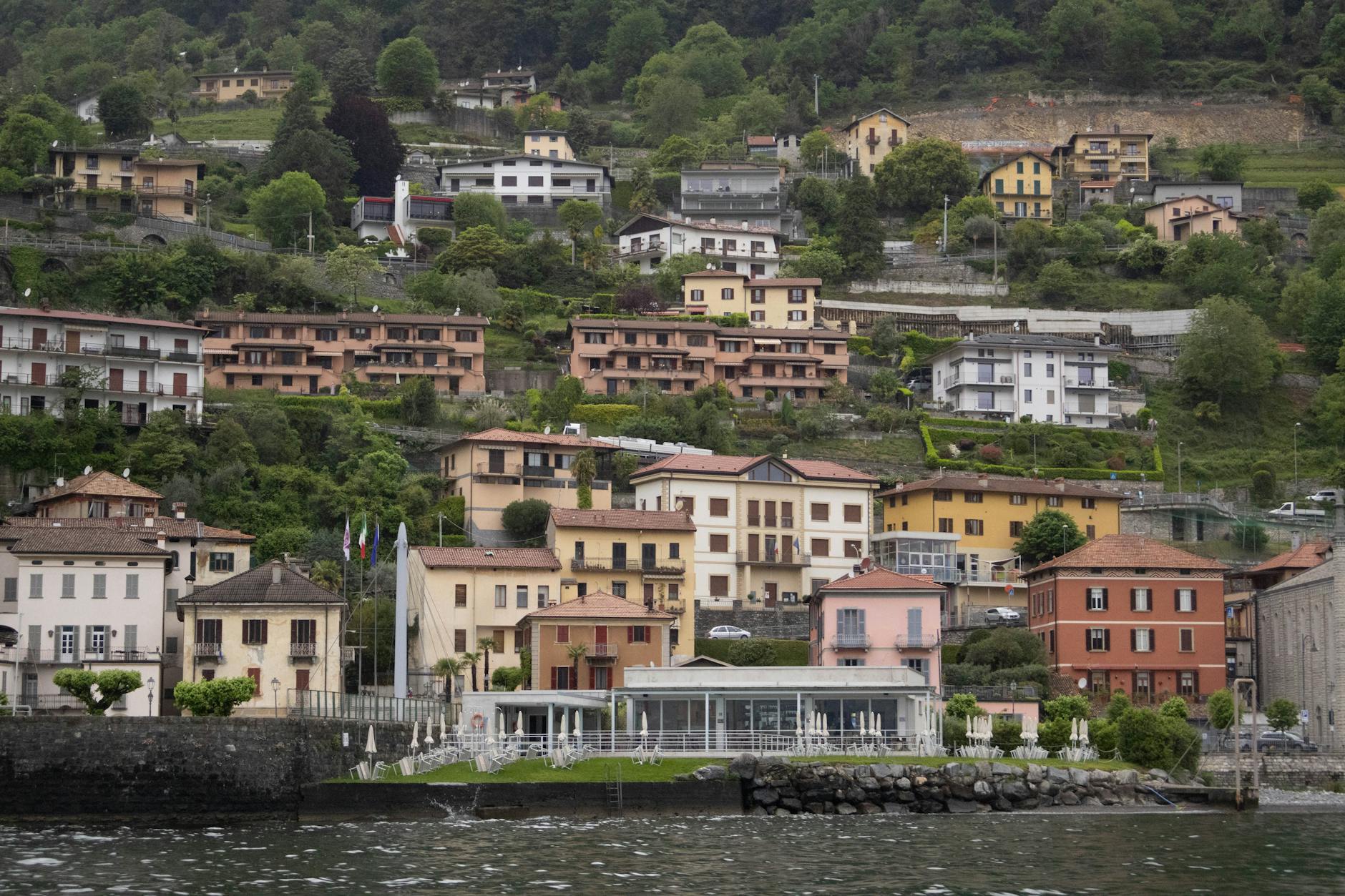 Charming hillside houses by Lake Como with lush greenery in Italy, perfect for travel enthusiasts.