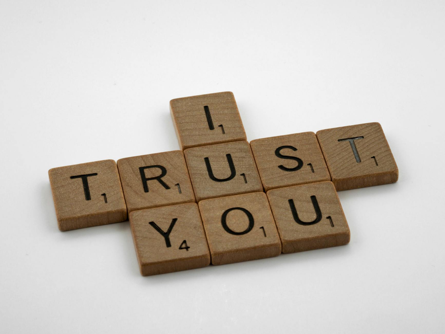 Close-up of Scrabble tiles arranged to spell 'I Trust You' on a white background, symbolizing trust.