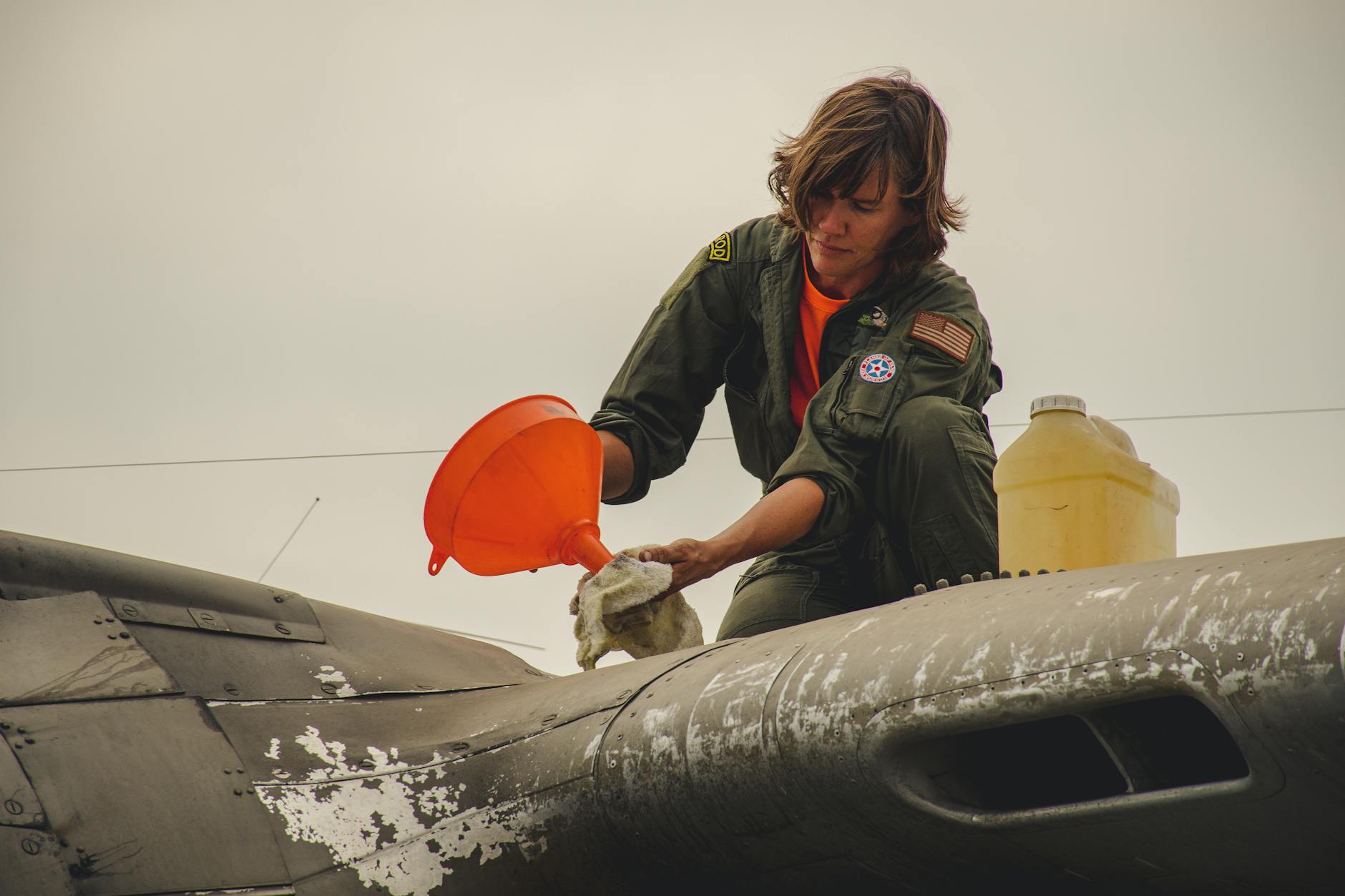 Crew member performing maintenance on an aircraft with a funnel outdoors.