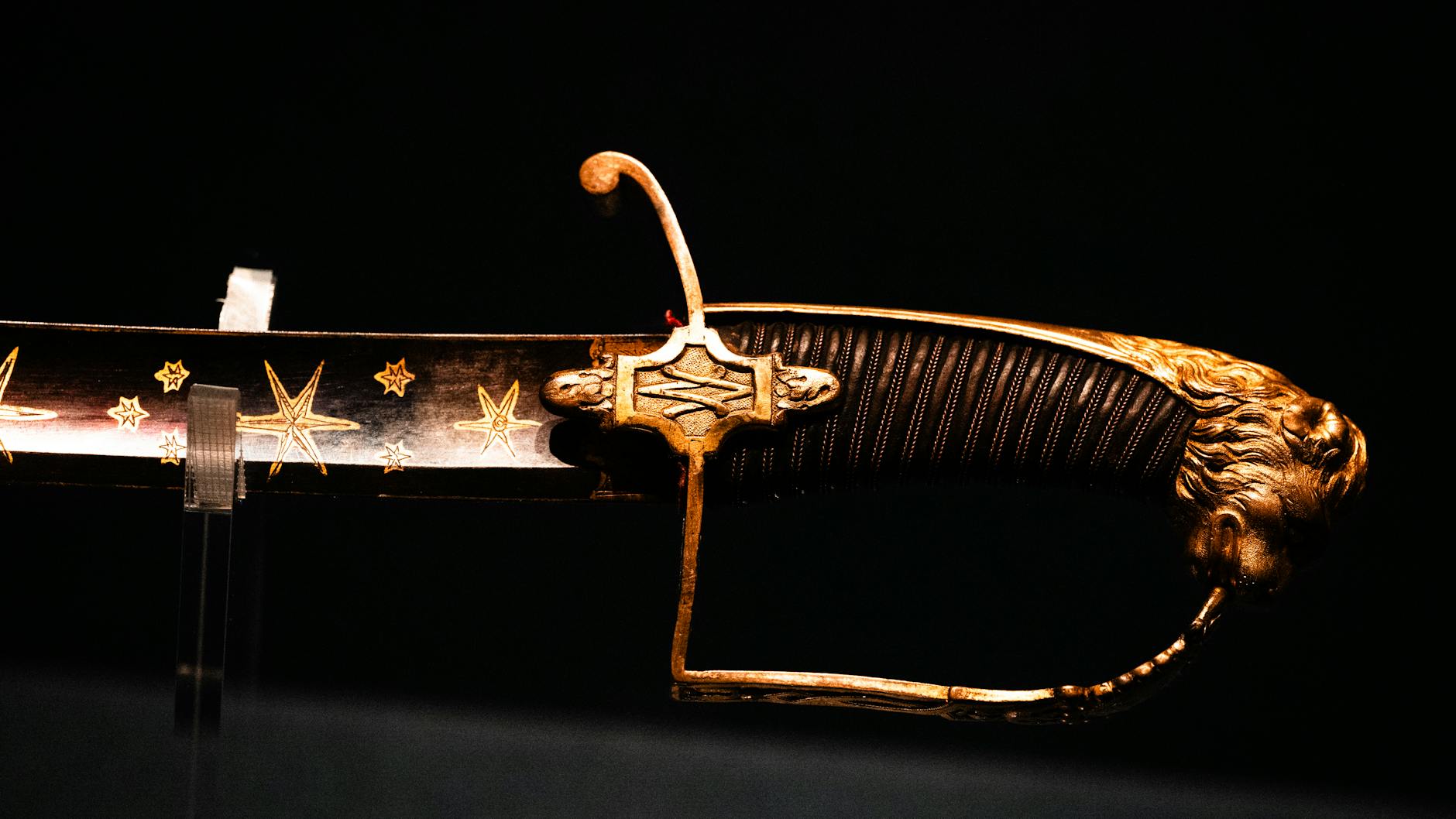 Detailed close-up of a historical saber with ornate gold embellishments and star motifs on its blade.