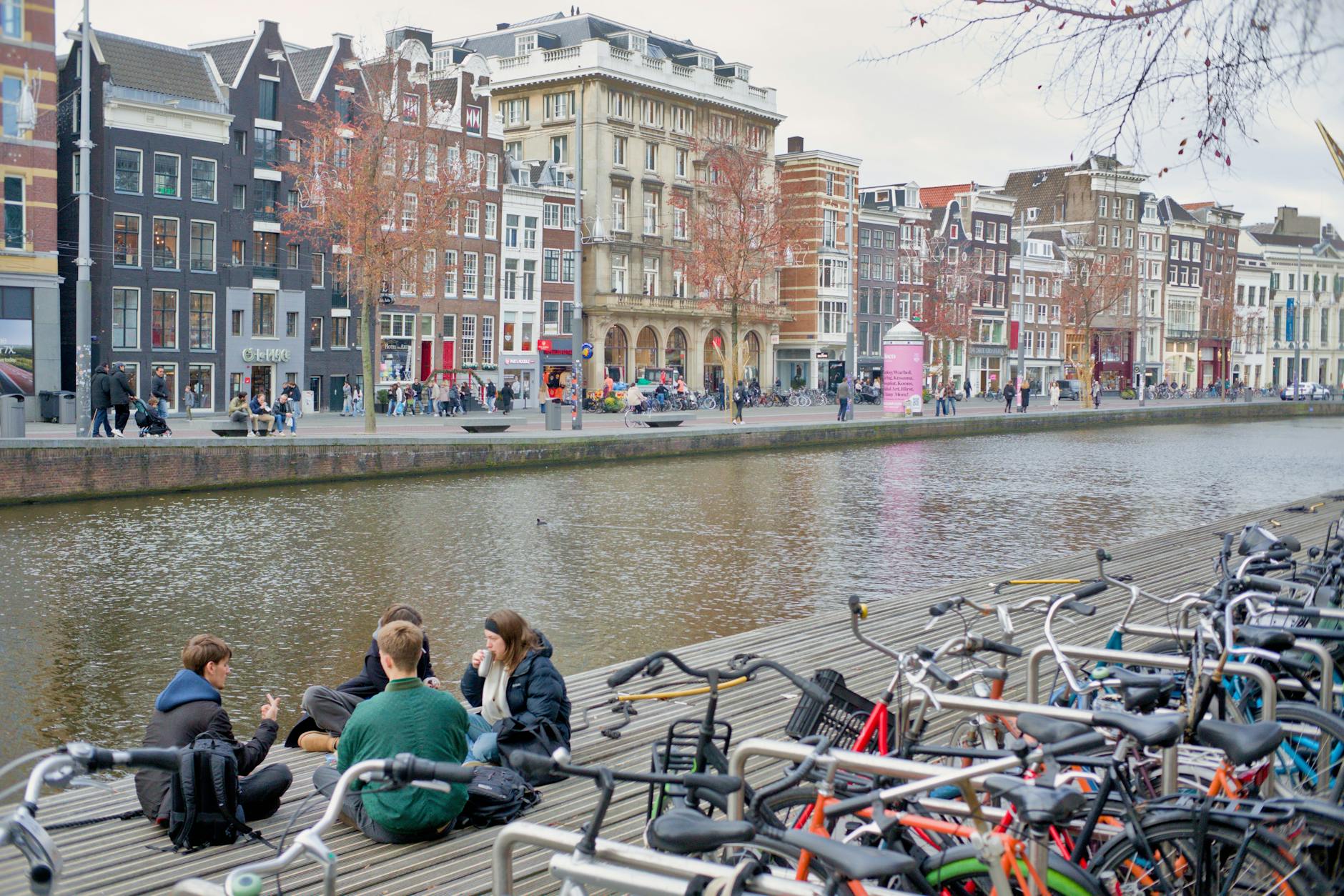 Group of friends enjoy a relaxing day by a canal in Amsterdam, with bikes nearby.