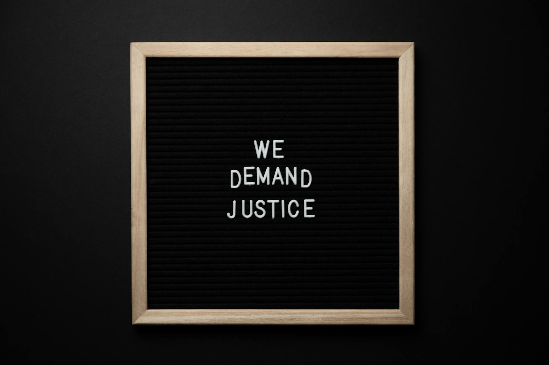 Sleek protest sign with 'We Demand Justice' text on black felt board. Minimalist design.