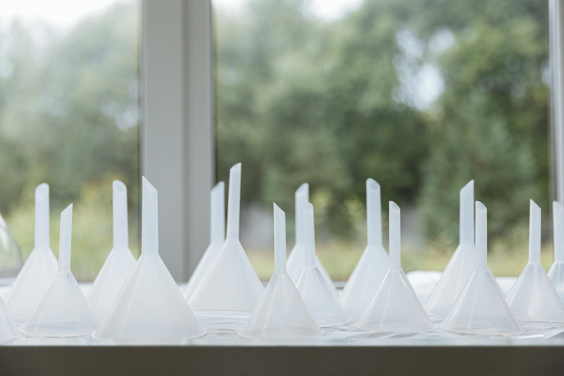 White plastic funnels arranged near a window with greenery outside.