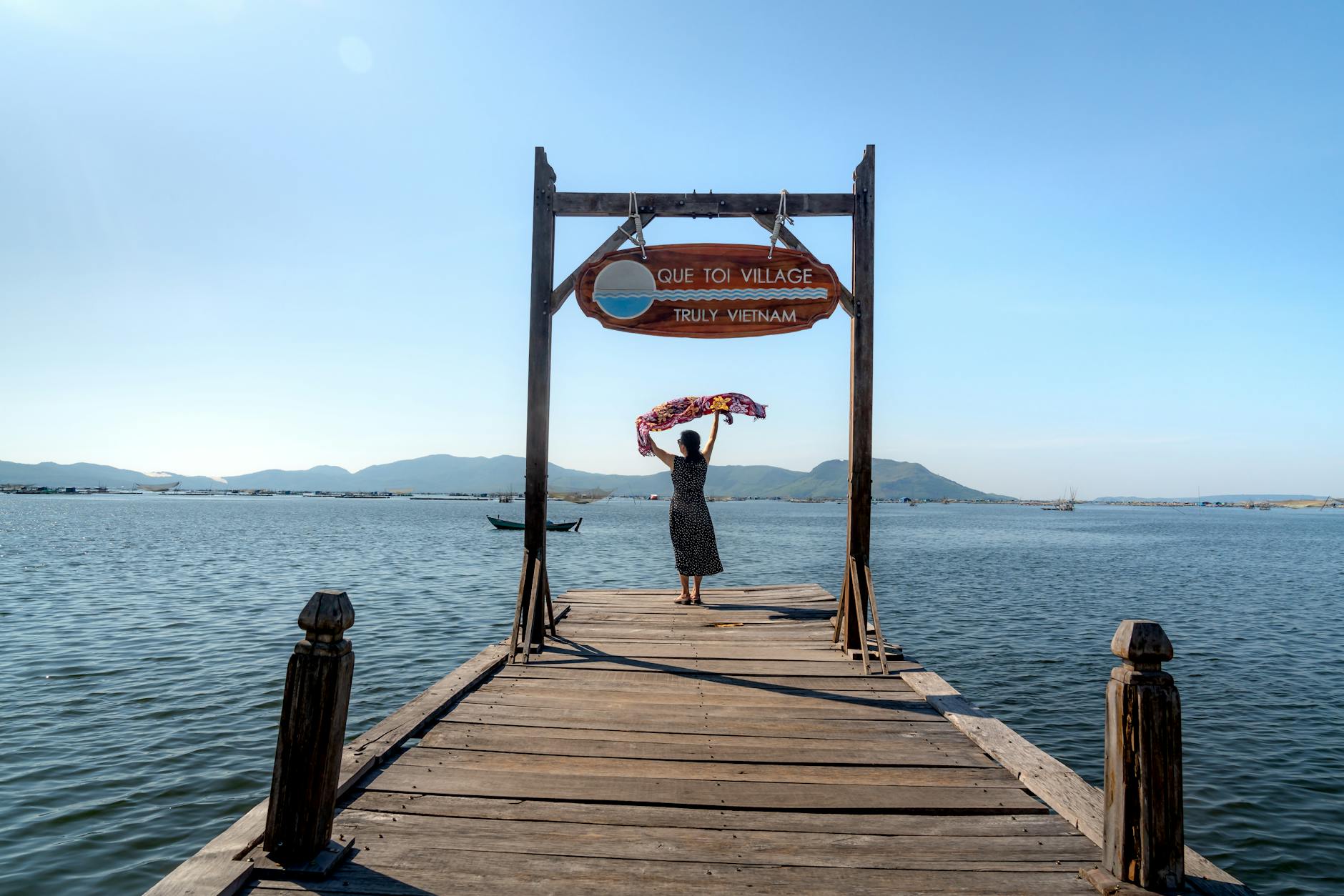 Woman on a wooden dock with a scarf overlooks the sea at Que Toi Village, Vietnam.