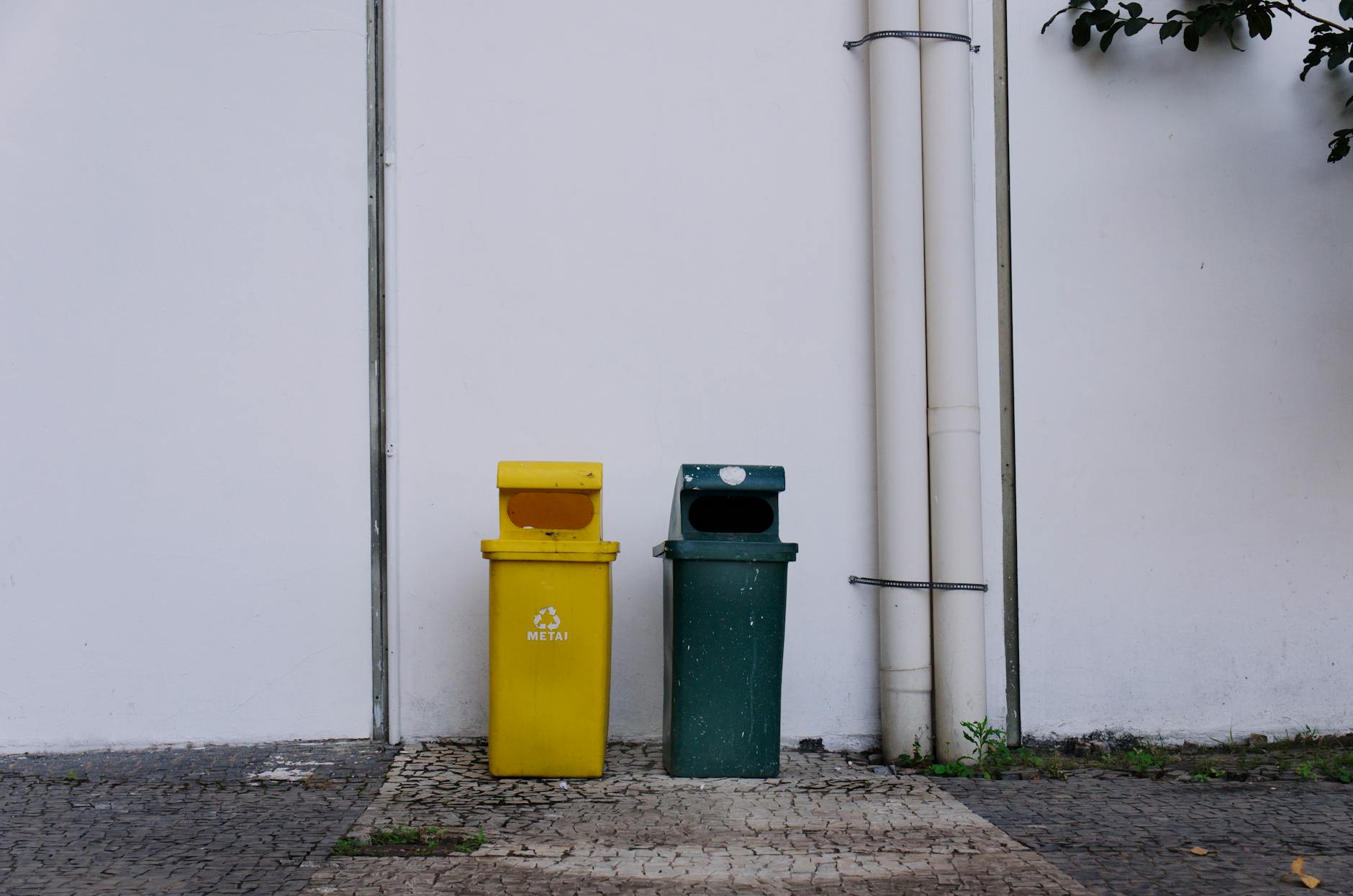 Yellow and green recycling bins beside a white wall in Juiz de Fora, Brazil.